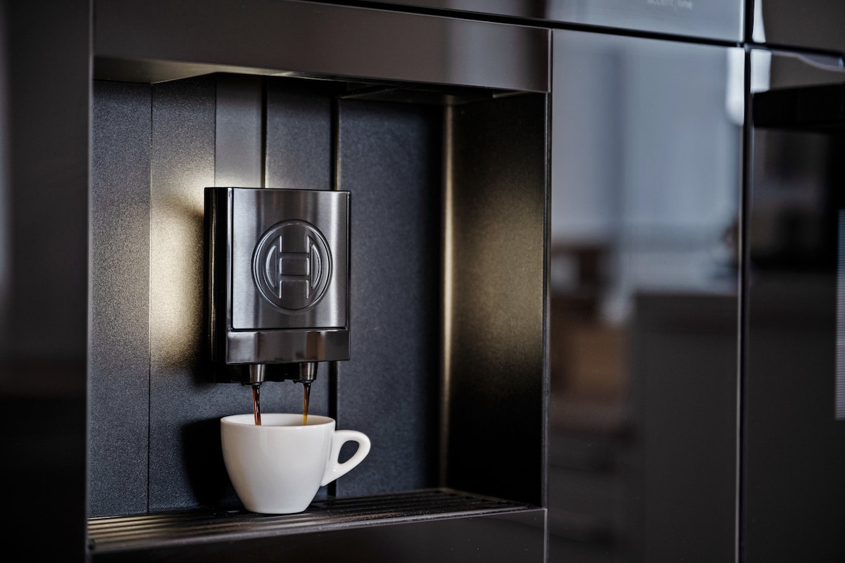 Integrierte Kaffeestation mit einer Tasse unter dem Auslauf vor dunkler Wand.